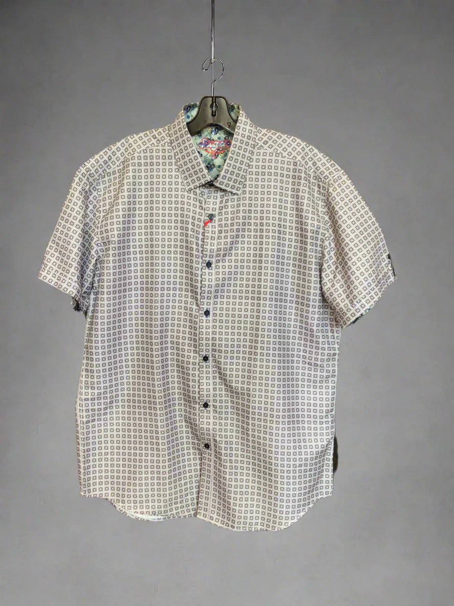 White shirt with black pattern on a black drying rack against a wooden wall.